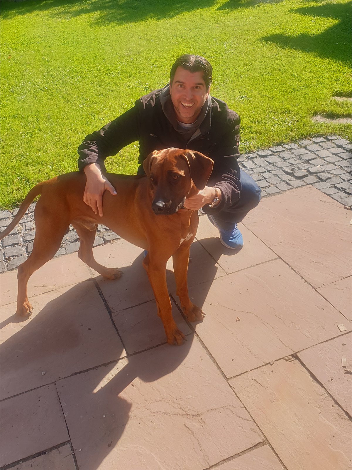 Bijan Maurer mit einem großen braunen Hund im Garten
